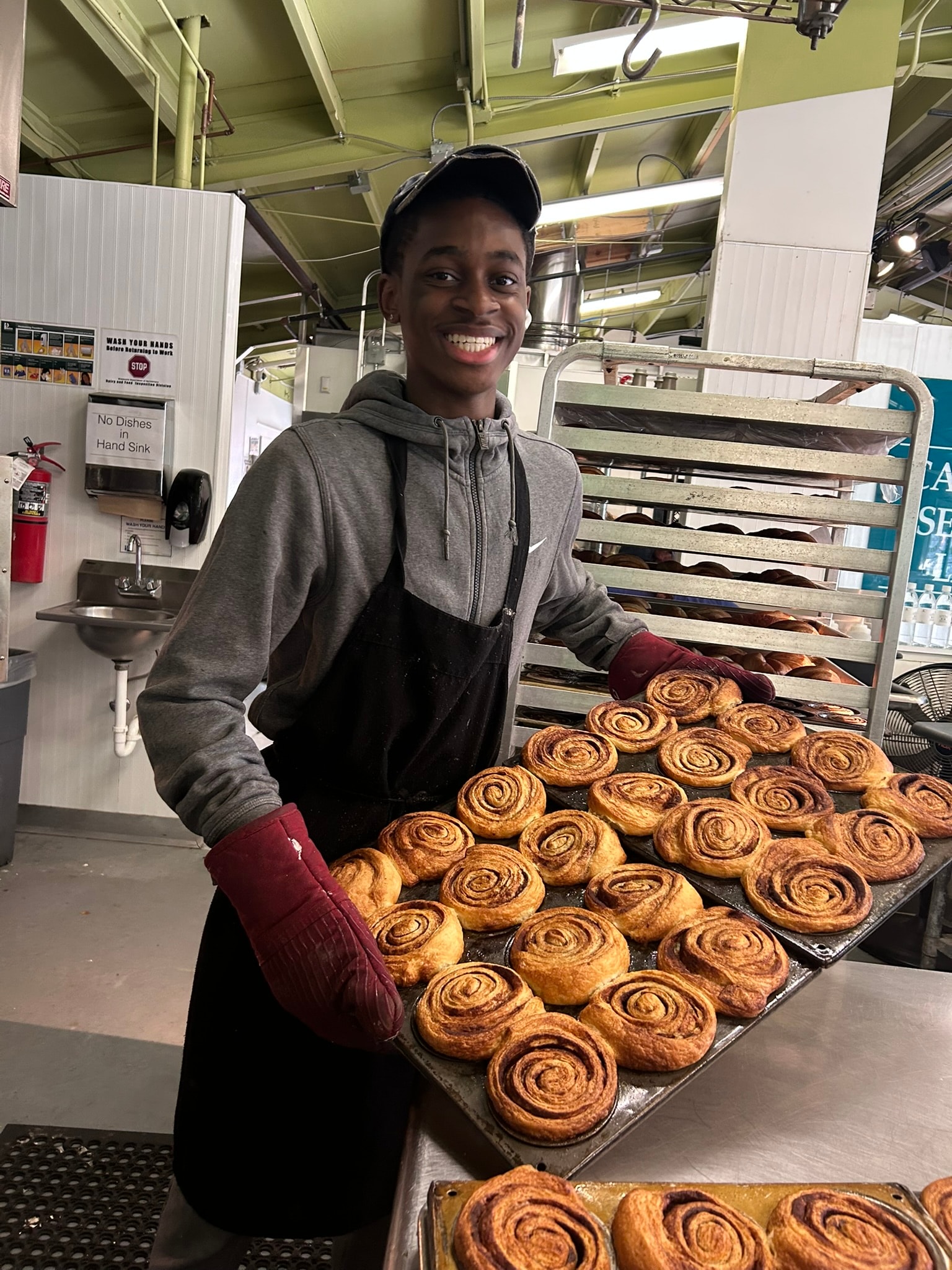 French Meadow staff member proudly holding a large tray of freshly baked cinnamon rolls straight from the oven